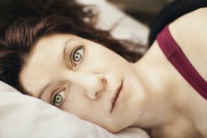 Vrouw die ligt te peinzen in bed. Wanneer we emoties niet goed verwerken, dan leidt dat vaak tot piekeren.